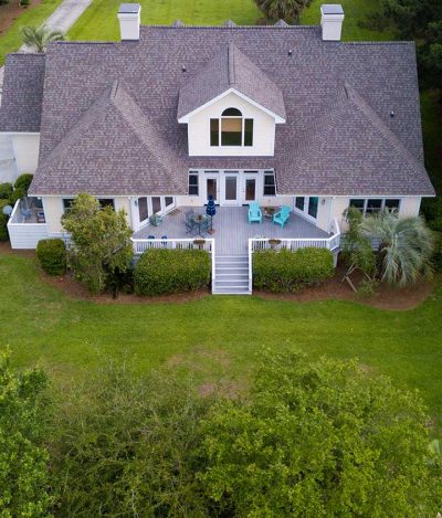 Aerial view of large home with new roof on wooded grassy property